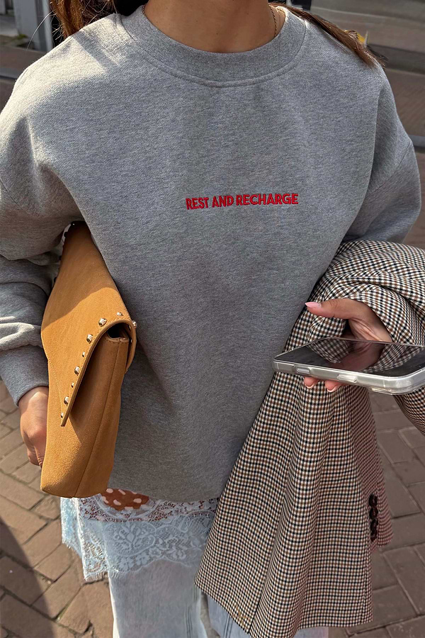 Grey Rest and Recharge Jumper with red embroidered text, styled with a tan suede bag and a checked blazer.