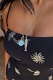 Deloris I Love You Necklace with a thin brass chain and spinning pendant, layered over a black palm tree dress.