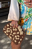 Jaden Beaded Clutch Bag with brown and cream pattern and crochet ball accents, held against a colourful print.