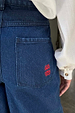 Blue Denim Pallazzo Jan Jean back pocket detail with a red embroidered logo and white shirt sleeve.