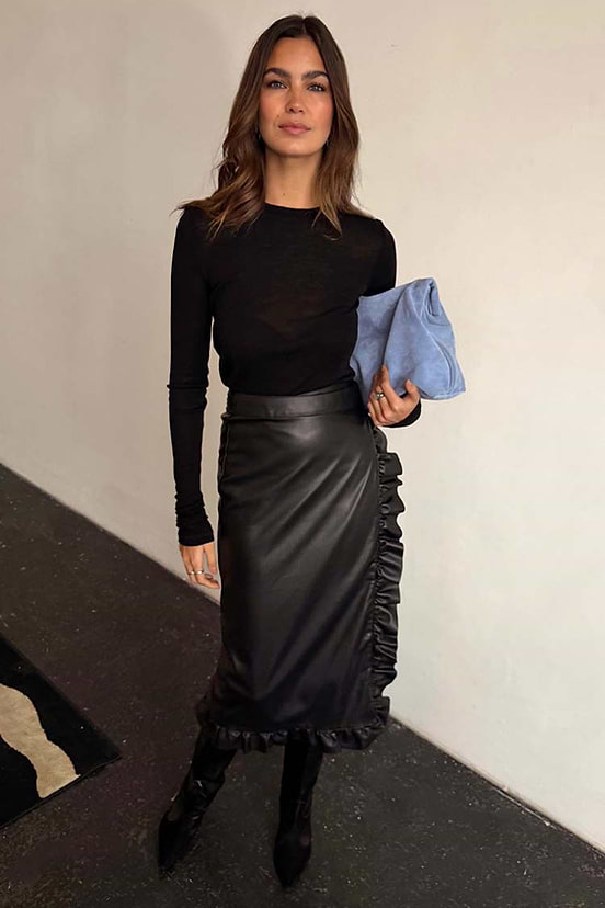 Black Vegan Leather Ruffle Jaspre Skirt featuring side frills, paired with a black long-sleeve top and blue clutch.