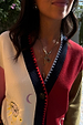 Deloris Key Necklace in brass with a red gemstone pendant, layered over a sun-embroidered cardigan.