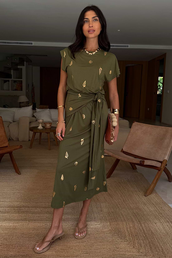 Khaki Shell Midi Dress with a gold seashell print and tie waist, shown on a model in a relaxed indoor setting.