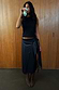 Thumbnail for Black Vegan Leather Wrap Skirt featuring a tulip tie detail, styled with a sleeveless top and boots.