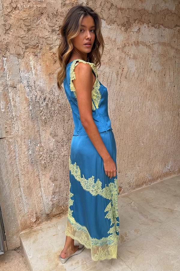 Blue satin Millie Skirt with lemon lace detailing and an asymmetric hem, styled as a co-ord against a rustic wall.