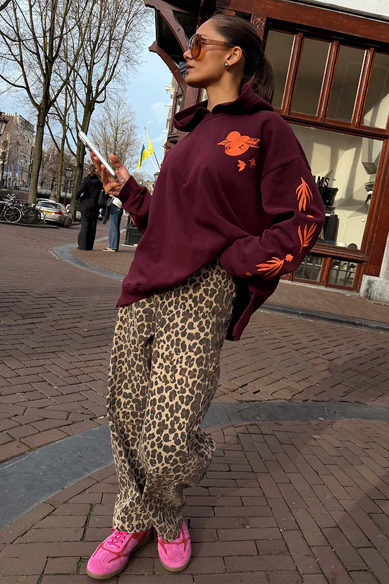 Leopard Barrel Jeans with an iconic print and relaxed barrel leg, styled with a burgundy hoodie for a street style look.
