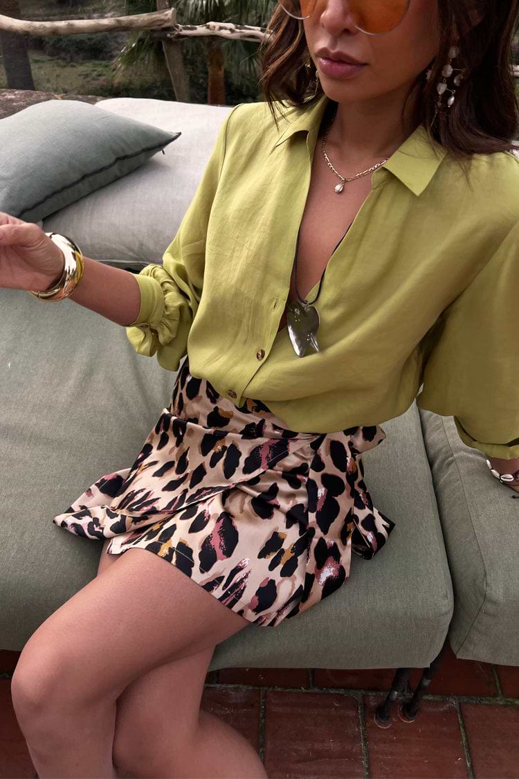 Model wearing a leopard mini Jaspre wrap skirt and lime green shirt while sitting outdoors.