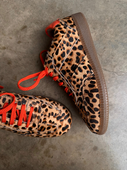 Leopard Pony Trainer featuring textured leopard print, vibrant orange laces, and a gum sole on a concrete surface.