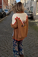 Tan Cowgirl Martha Cardigan with embroidered cowgirl motifs and red stitching, seen on a cobbled London street.