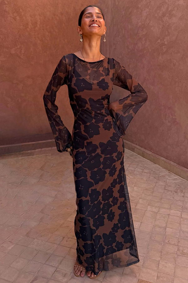 Tan Jaden Floral Mesh Maxi Dress with flared sleeves and a high neckline, worn against a terracotta background.