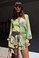Isla Miley Shirt and ruffle shorts in the green hand-painted Isla print, styled with sunglasses and a straw bag.