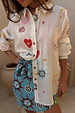 Sheer cream Morocco Charms Marley Shirt with heart and sun motifs, styled with a vibrant blue printed wrap skirt.