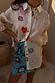 A Morocco Mini Wrap Skirt with blue sun prints layered under a white patterned button-down shirt.