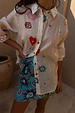 A Morocco Mini Wrap Skirt with blue sun prints layered under a white patterned button-down shirt.