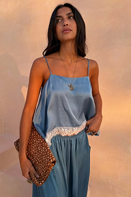 Deloris Thin Chain I Love You Necklace in brass with a spinning pendant, styled with a blue lace-trim top and spotted clutch.