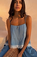 Deloris I Love You Necklace in gold brass with a spinning pendant, worn on vacation with a blue lace-trimmed top.