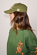 Olive Amara Cap in green cotton with white embroidery, styled with a matching green graphic sweatshirt.