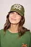 Olive Amara Cap in olive green cotton with white heart embroidery, worn with a matching crew neck sweatshirt.