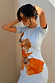 Orange Acetate Visor Sunglasses with tinted lenses, worn by a model in a blue floral graphic print dress.