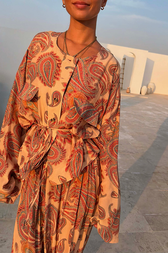 Peach Paisley Anna Top with a button-through front and tie waist, worn in a sunny outdoor terrace setting.
