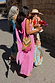 Pink Sophie Dress featuring gold flecks and a multi-wear scarf, styled with a beaded bag on a sunny cobbled street.