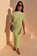 Pistachio Tilly Dress in green plisse with gold flecks and a lettuce hem, styled off-the-shoulder on stairs.