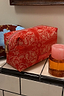 Thumbnail for Red Bandana Reversible Make Up Bag with a cream paisley print and gold zipper, shown on a tiled bathroom ledge.