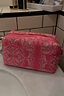 Pink bandana print reversible makeup bag with a gold zip closure, sitting on a marble bathroom counter.