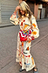 Thumbnail for Cream Poema Shirt Dress with colourful motifs, an orange lettuce trim and ruffle hem on a cobblestone street.