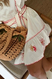 Pollenca Mini Dress in cream cotton with red sun embroidery and a tiered skirt, paired with a woven palm bag.