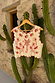 Cream Pollenca Top with red palm tree embroidery and scallop edge trim, hanging against a cactus background.