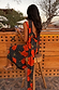 Black Poppy Sophie Dress in a red poppy and polka dot print with a low cowl back and detachable scarf at an outdoor bar.