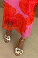 Pink Poppy Mesh Dress featuring a vibrant red floral print, styled with metallic gold flower-adorned sandals.