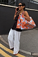 Two Blue Poppy Gift Bags with an orange floral print, carried by a model in a London street style look.
