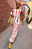 Thumbnail for Cream Marina Marra Trousers and matching waistcoat in a red fish print, styled for a vacation in a narrow street.