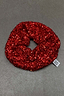 Red Sequin Scrunchie with shimmering sequins and a branded tag, a festive accessory for a London look.