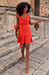 Tomato Mini Sophie Dress in red featuring a cowl neckline and multi-wear scarf, styled on a model on stone steps.
