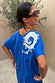 Red Wiggle Arm Acetate Sunglasses with red tortoise frames and dark lenses, worn with a blue graphic t-shirt.