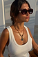 Red tortoise acetate sunglasses with wiggle arms and dark lenses, worn with a white ribbed vest and gold chain.