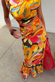 Rio A-Symmetric Skirt in a colourful tropical fruit print, styled with a matching top and red bag for a vacation look.