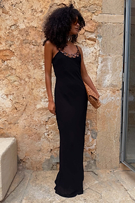 Black Sapna maxi dress with ring detailing at the neckline and a fitted silhouette against a stone wall.
