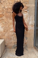 Black Sapna maxi dress with ring detailing at the neckline and a fitted silhouette against a stone wall.
