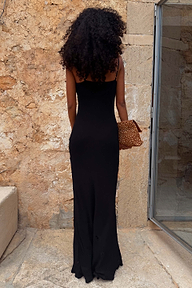 Sleek black Sapna maxi dress with adjustable straps and a fitted silhouette, shown from the back against a stone wall.