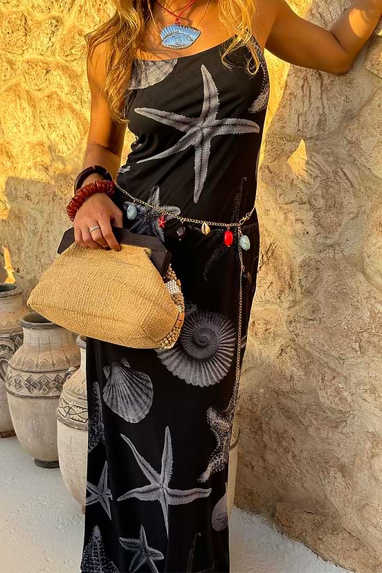 Black Seashell Mesh Cami Dress with white starfish print, styled with a charm belt and straw bag against a stone wall.