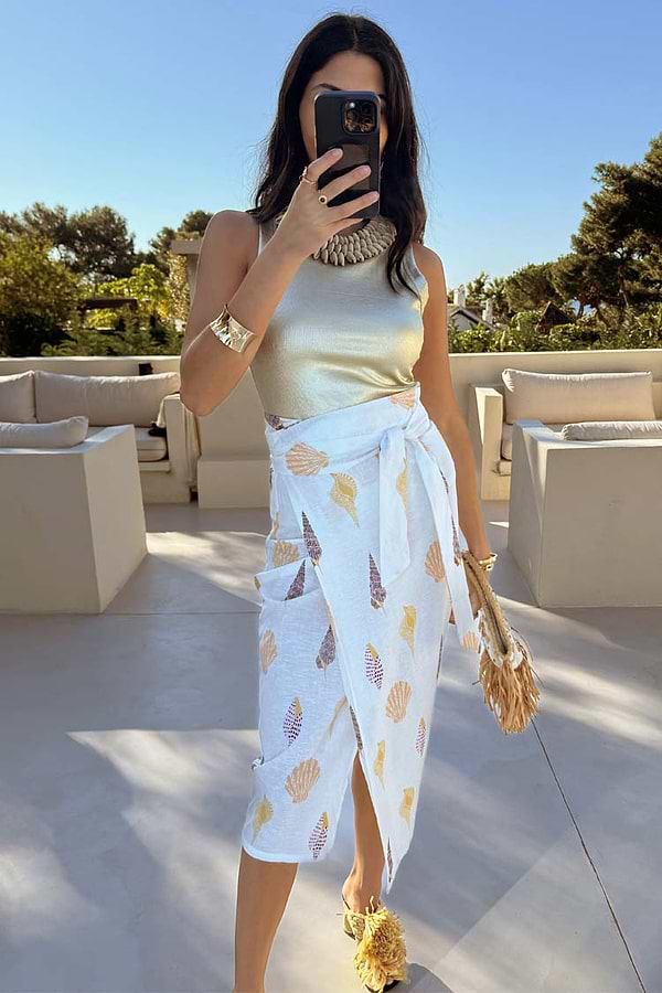 White Shells Jaspre Wrap Skirt featuring a shell print and wrap tie, styled with a gold top for a vacation look.