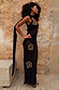 Black & Gold Simona Sequin Maxi Dress in sheer mesh with a trailing scarf, styled on a model against a stone wall.