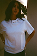 White cotton T-shirt with silver stud detailing around the neckline and a relaxed fit on a model.