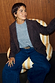 Chocolate Suede Jacket styled over a grey jumper and denim jeans while seated in a striped armchair.