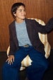 Chocolate Suede Jacket styled over a grey jumper and denim jeans while seated in a striped armchair.