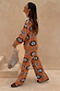 Tan Sun Trousers and matching knit jumper co-ord with sun and swirl motifs, walking on stone steps.